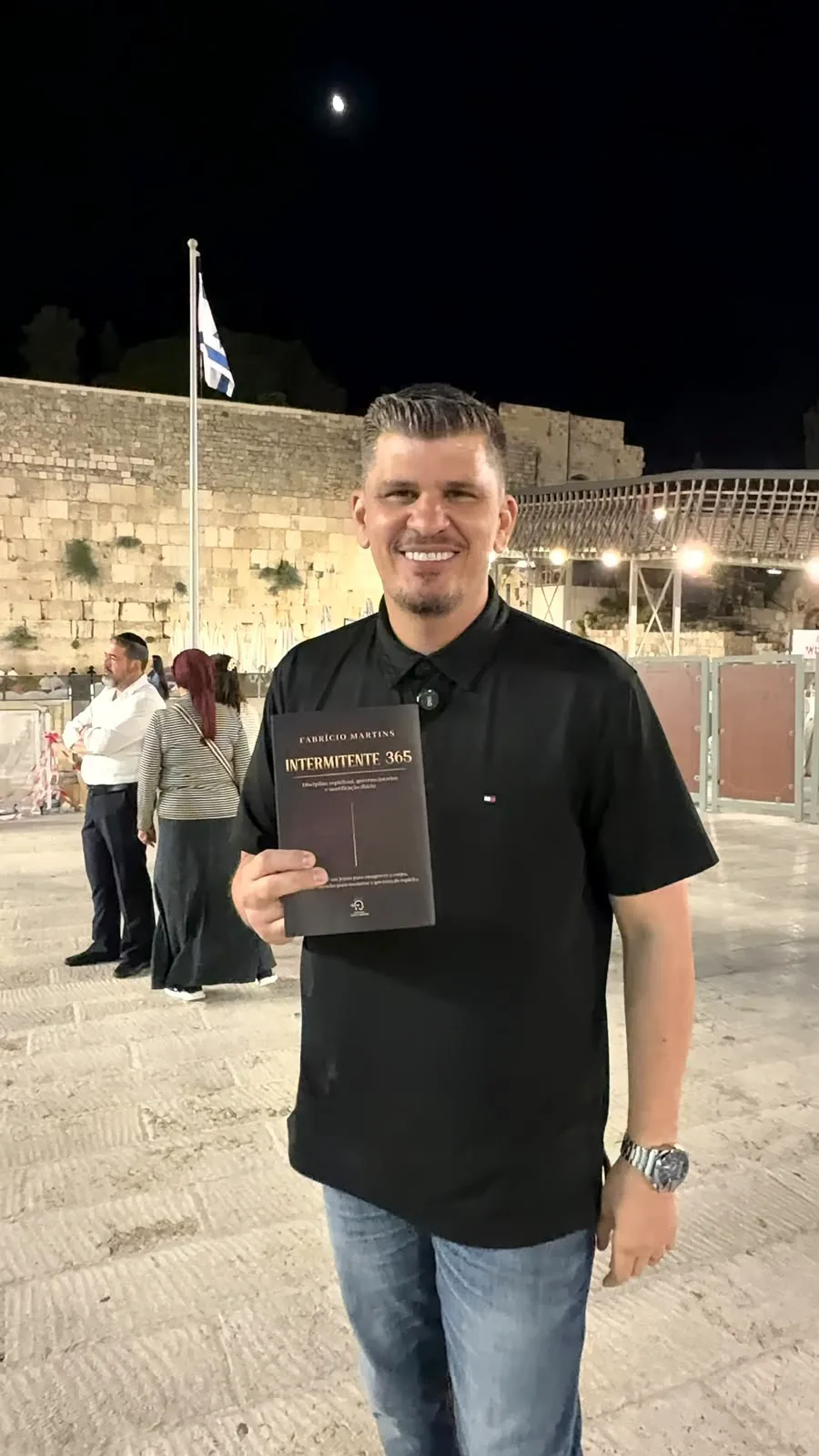 Fabrício Martins com o livro na praça do Muro das Lamentações, à noite